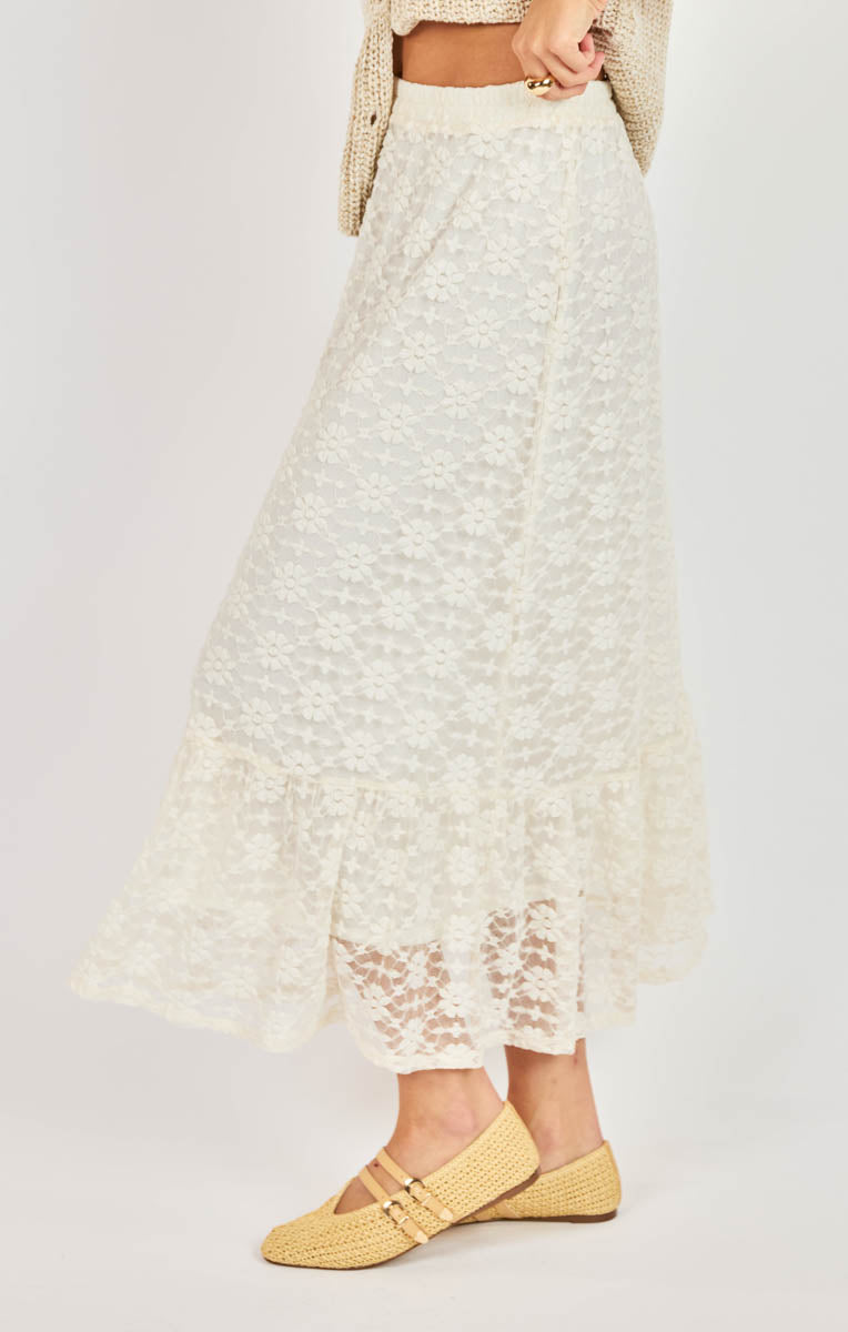 Person wearing a white lace skirt with yellow shoes on a plain background