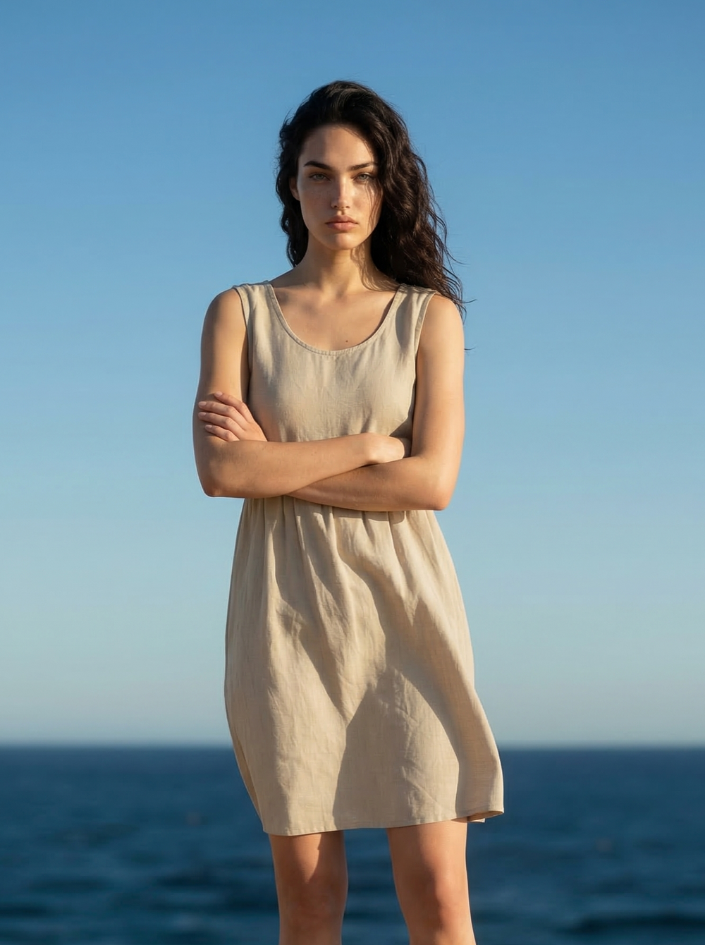 Woman in a beige dress standing against a blue sky and ocean.