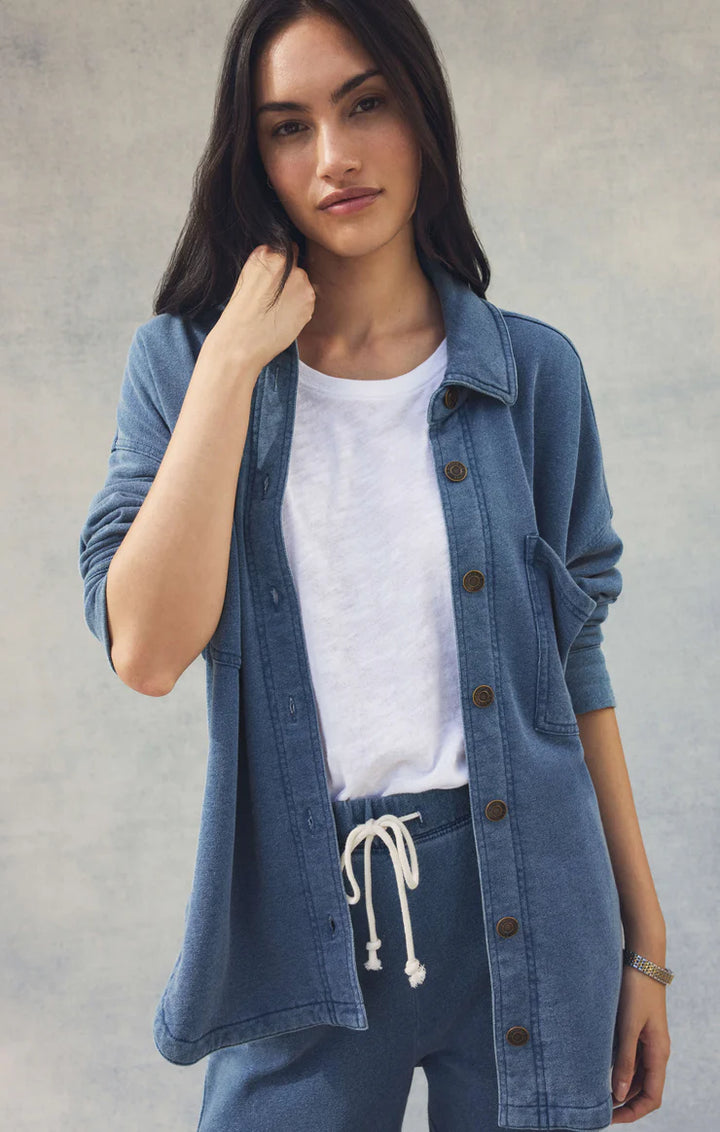 Woman wearing a denim jacket over a white shirt and blue pants against a gray background