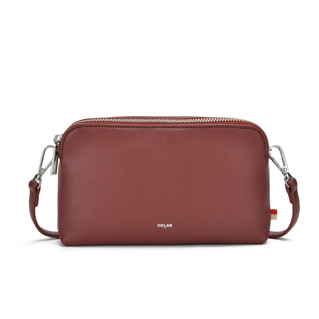 A reddish-brown pebbled leather crossbody bag with silver-tone hardware and a small white &
