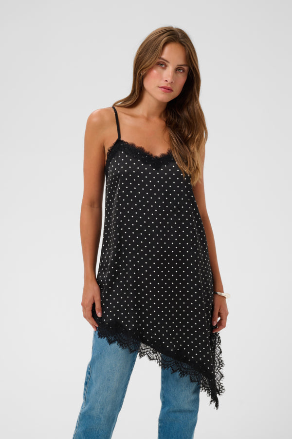 A woman modeling a black camisole top with white polka dots and lace trim, paired with blue jeans, against a plain light gray studio background.