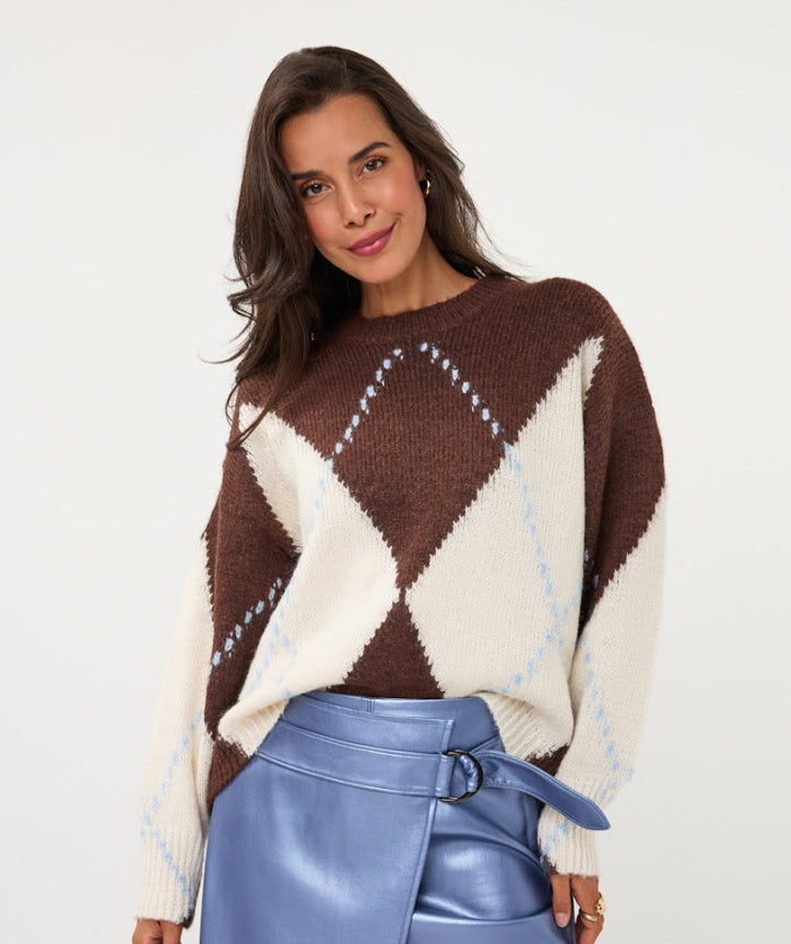A woman wearing a brown and cream argyle knit sweater with light blue diamond accents, paired with a shiny blue wrap skirt, against a plain white studio background.