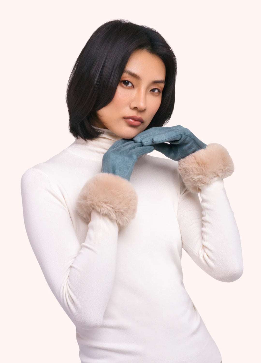Woman wearing white turtleneck and blue gloves with fur cuffs on a white background