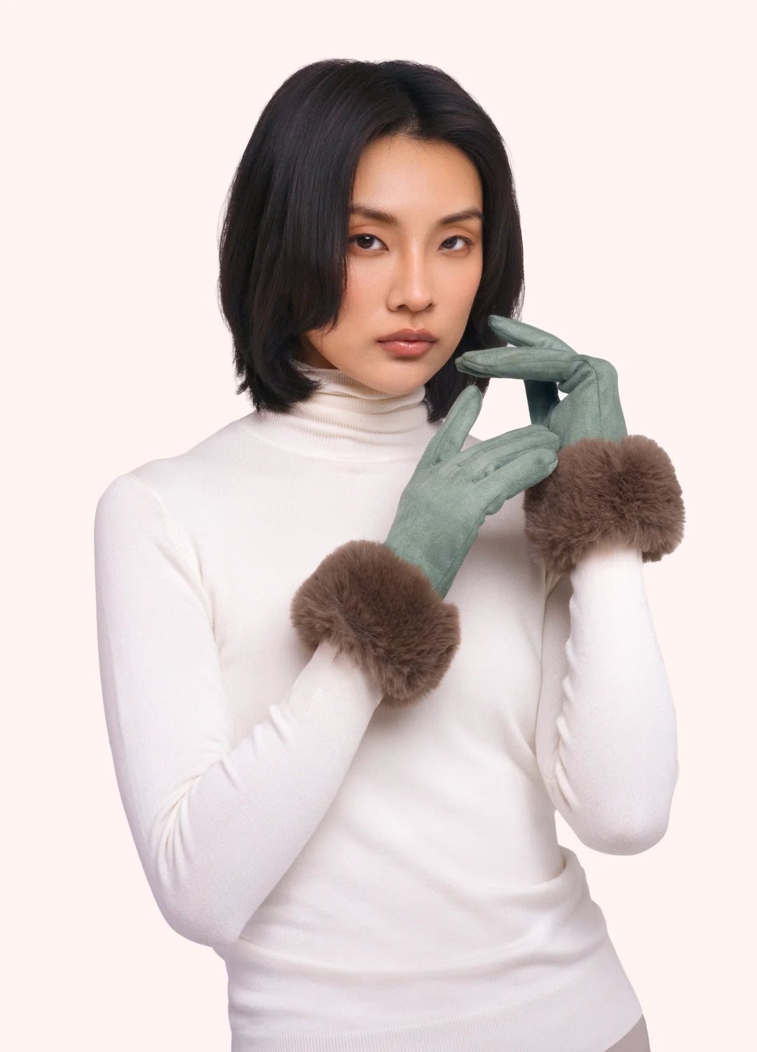 Woman wearing a white turtleneck and green gloves with fur cuffs on a white background