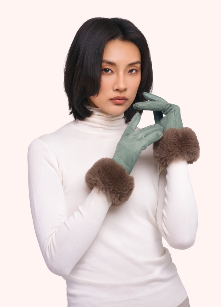 Woman wearing a white turtleneck and green gloves with fur cuffs on a white background