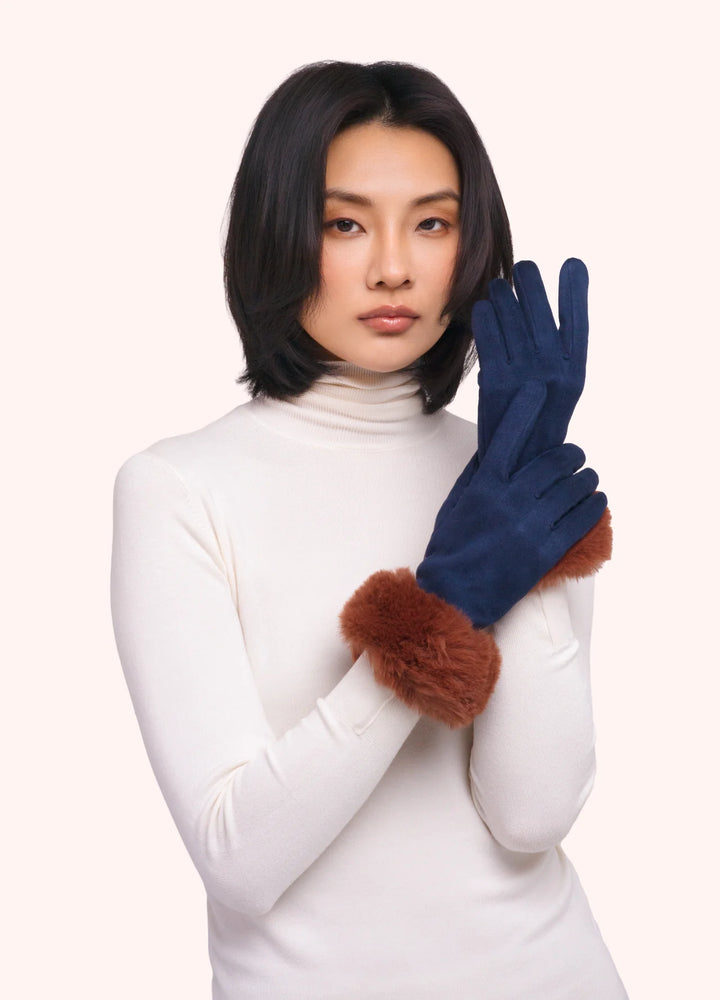 Woman wearing navy gloves with brown fur cuffs on a white background