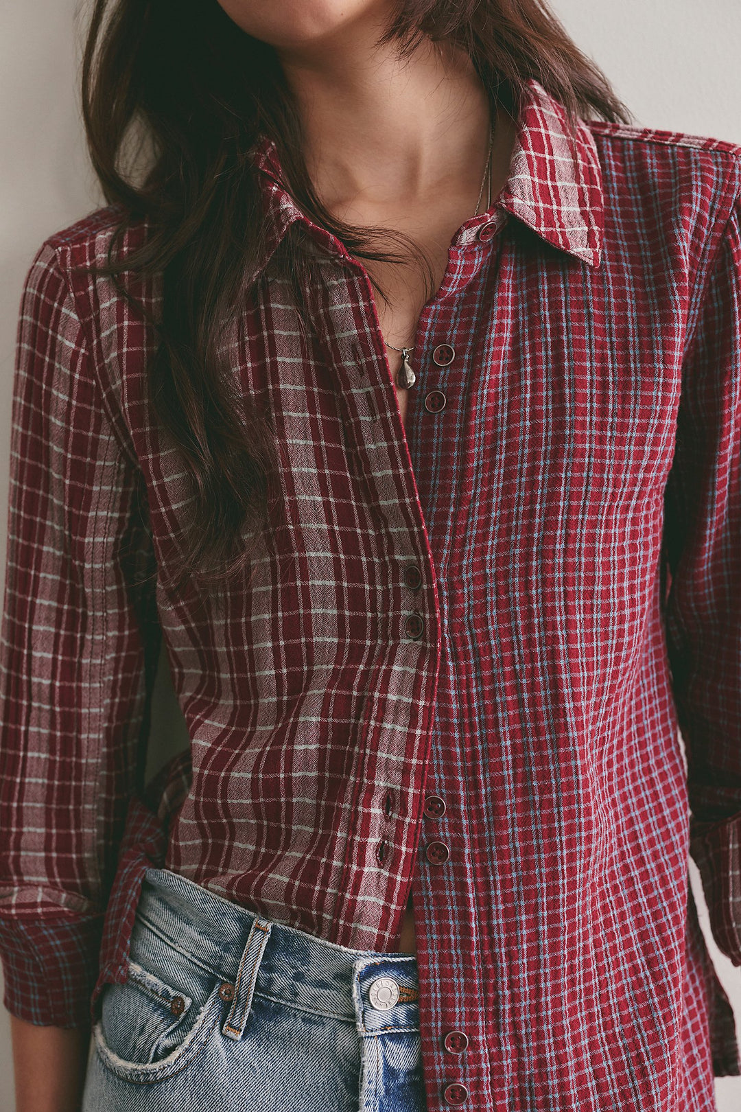 A close-up of a person wearing a red and dark plaid button-up shirt tucked into blue jeans.