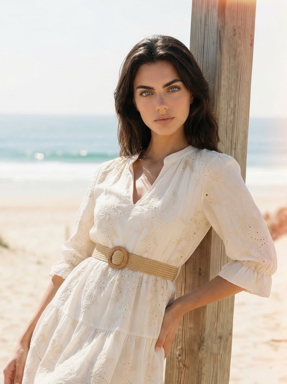 Woman in a white dress standing on a sandy beach with ocean view