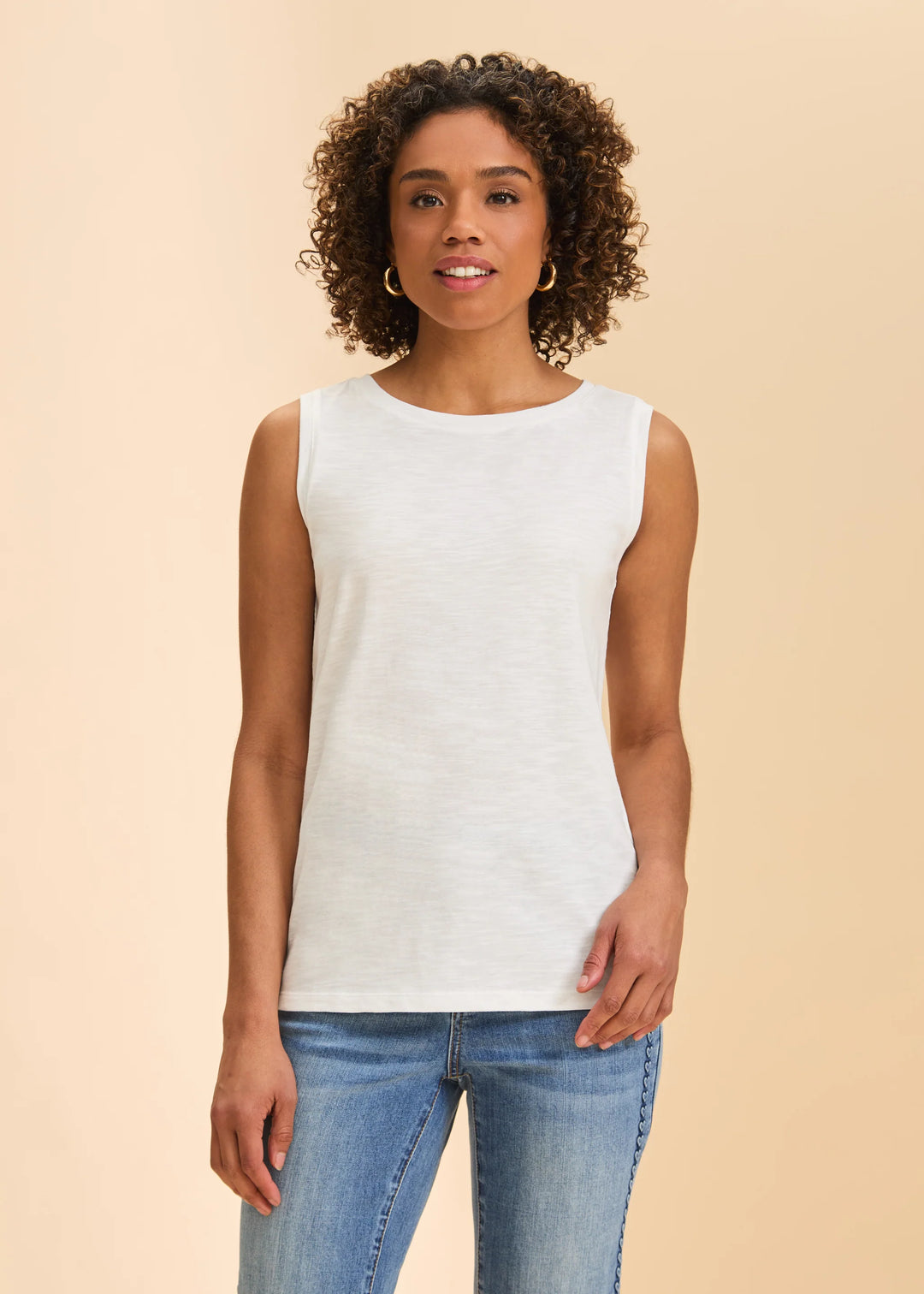Woman wearing a white sleeveless top and blue jeans on a beige background