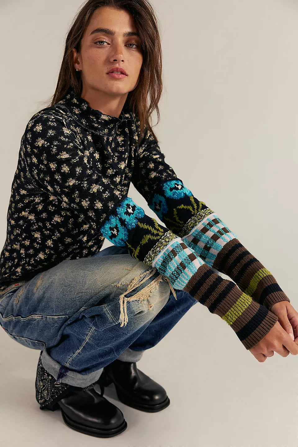 Person wearing a patterned sweater with colorful sleeves and jeans, sitting on the ground.