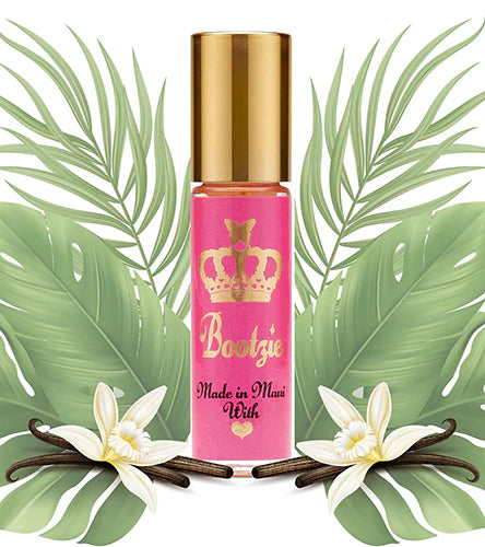 A small, roller ball bottle of Bootzie Oil with a pink label and a gold-colored cap, displayed on a background featuring green leaves and white flowers.