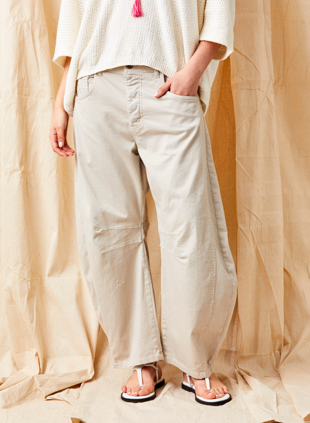 Person wearing light-colored pants and a white top against a beige curtain background