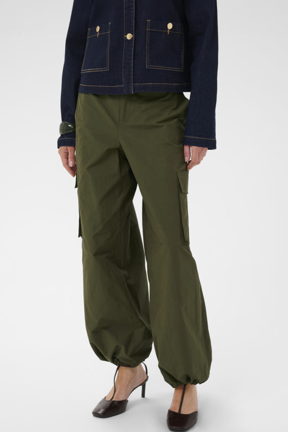 A model is shown from the waist down wearing olive green wide-leg cargo pants with gathered cuffs, styled with a dark denim jacket and black heels against a light gray studio background.
