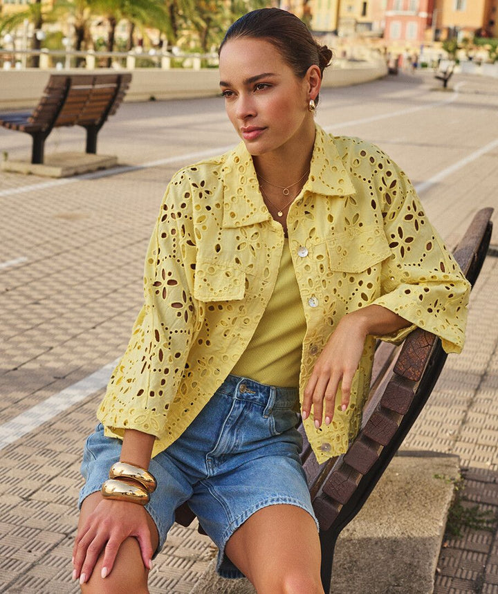 Woman wearing a yellow lace jacket sitting on a bench outdoors.