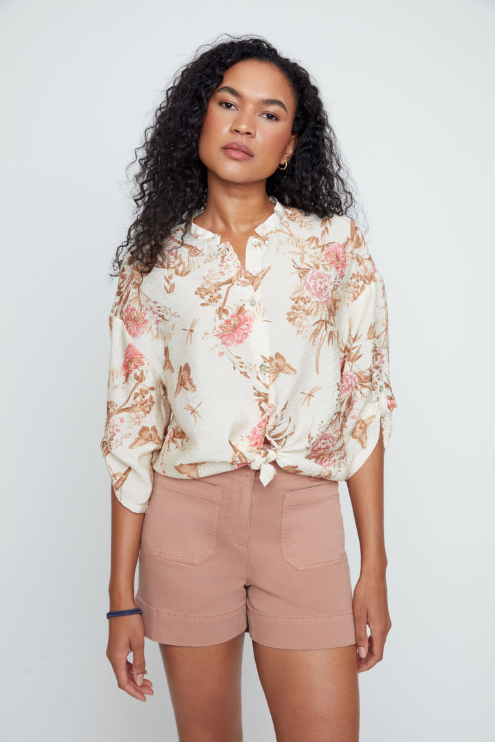 Woman wearing a floral blouse and beige shorts against a white background