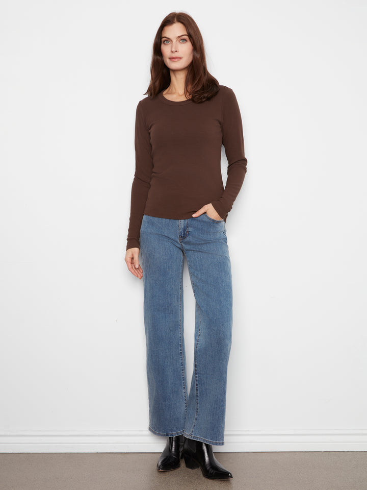 A woman modeling a brown long-sleeve crewneck top and wide-leg blue jeans against a plain white wall.