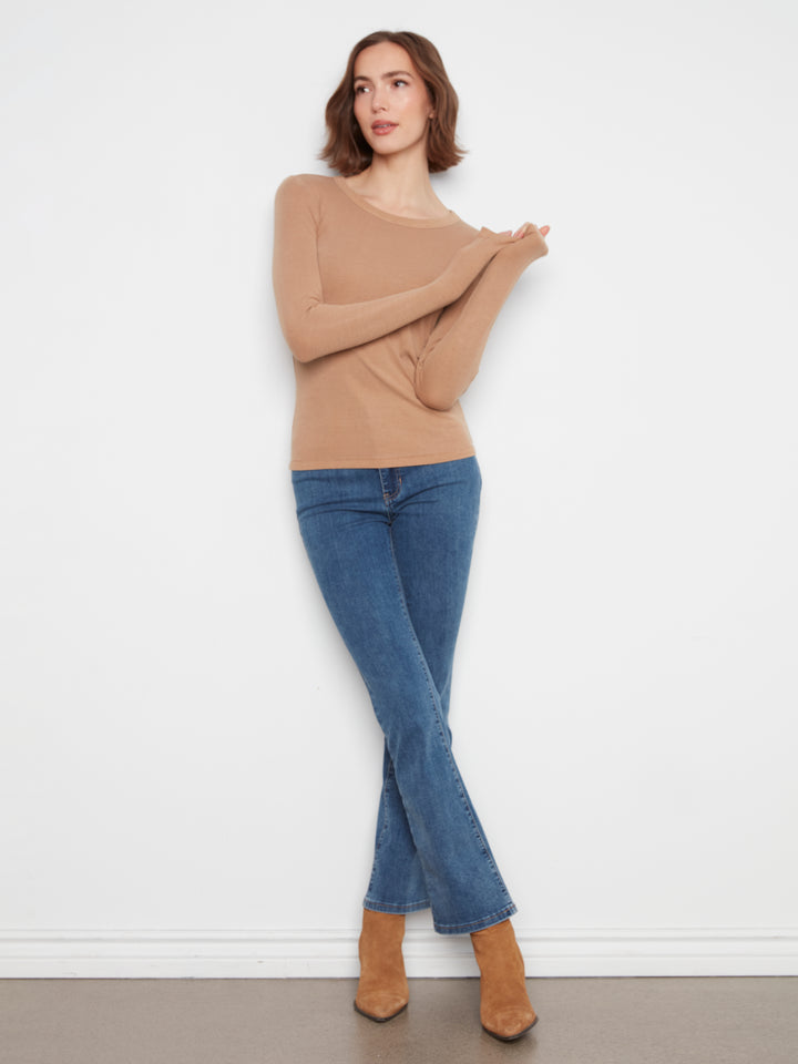 Woman wearing a beige sweater and blue jeans against a white background