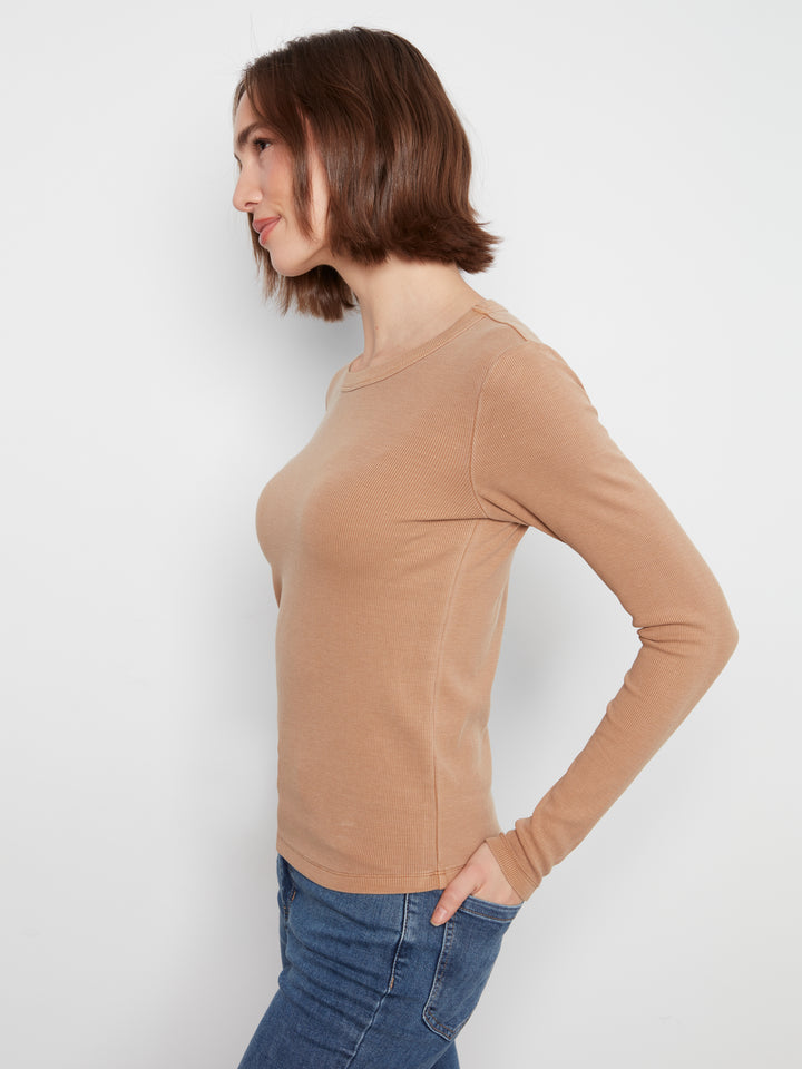 Woman wearing a beige long-sleeve top and blue jeans against a white background
