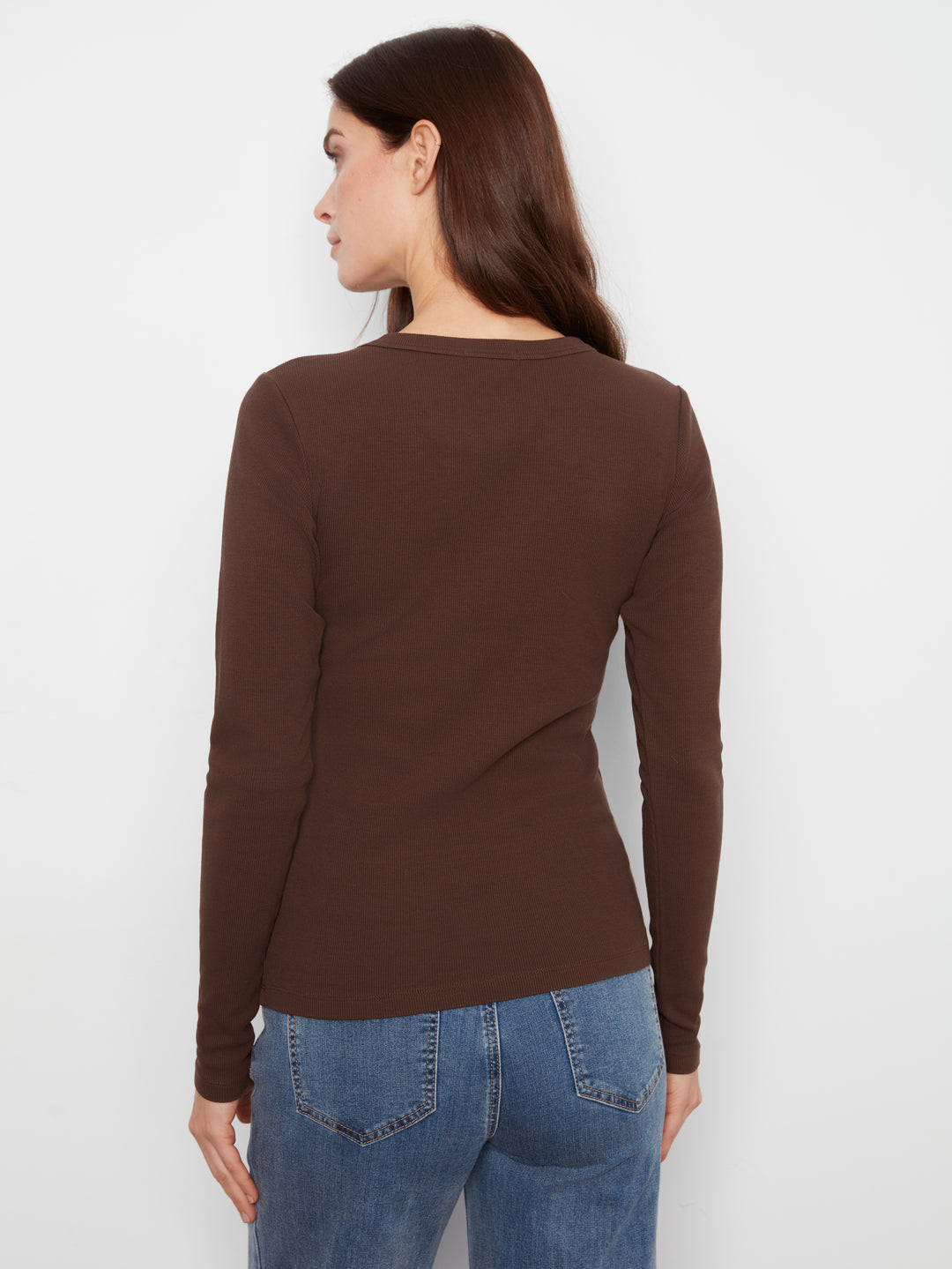 Woman wearing a brown long-sleeve top and blue jeans against a white background