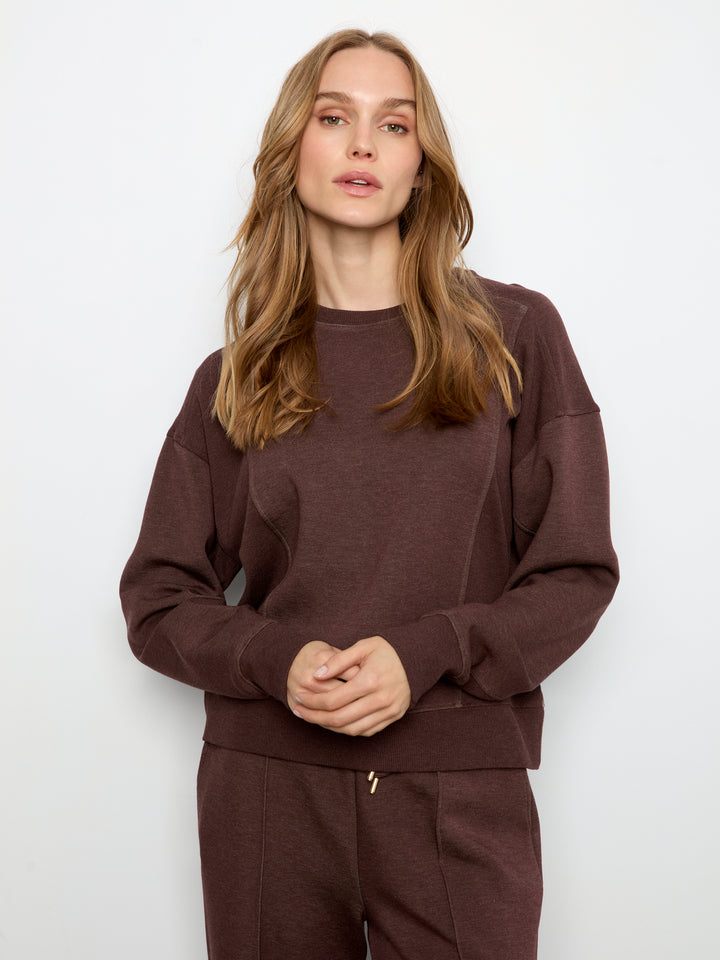 A woman modeling a dark brown crewneck sweatshirt and matching sweatpants against a plain white studio background.