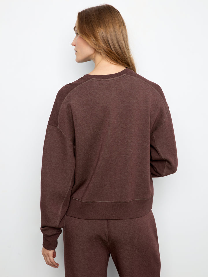 A woman shown from the back wearing a dark brown crewneck sweatshirt and matching sweatpants against a plain white studio background.
