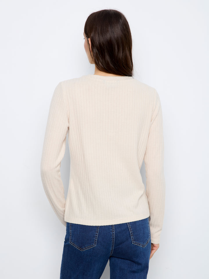 A woman viewed from the back wearing a cream ribbed long-sleeve top and blue jeans against a plain white background.