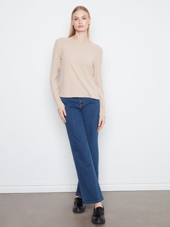 A woman modeling a beige ribbed long-sleeve mock neck sweater with dark blue wide-leg jeans and black loafers, standing against a white wall.