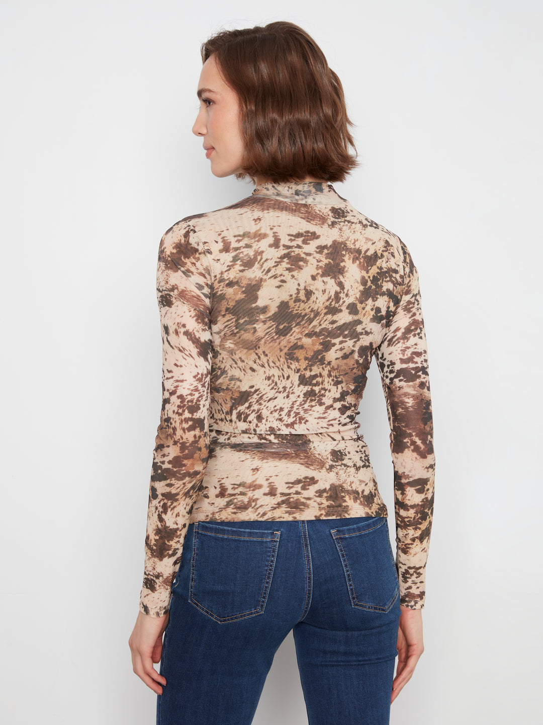 Woman wearing a camouflage long-sleeve top and blue jeans on a white background