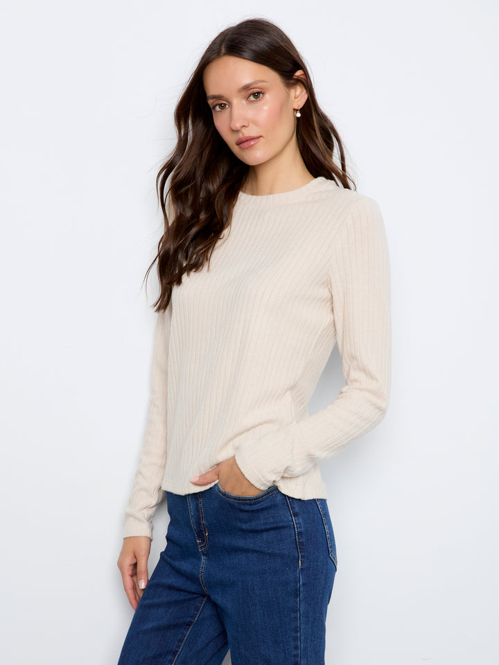 A woman modeling a cream ribbed long-sleeve crewneck sweater paired with dark blue jeans, photographed against a clean white studio background.
