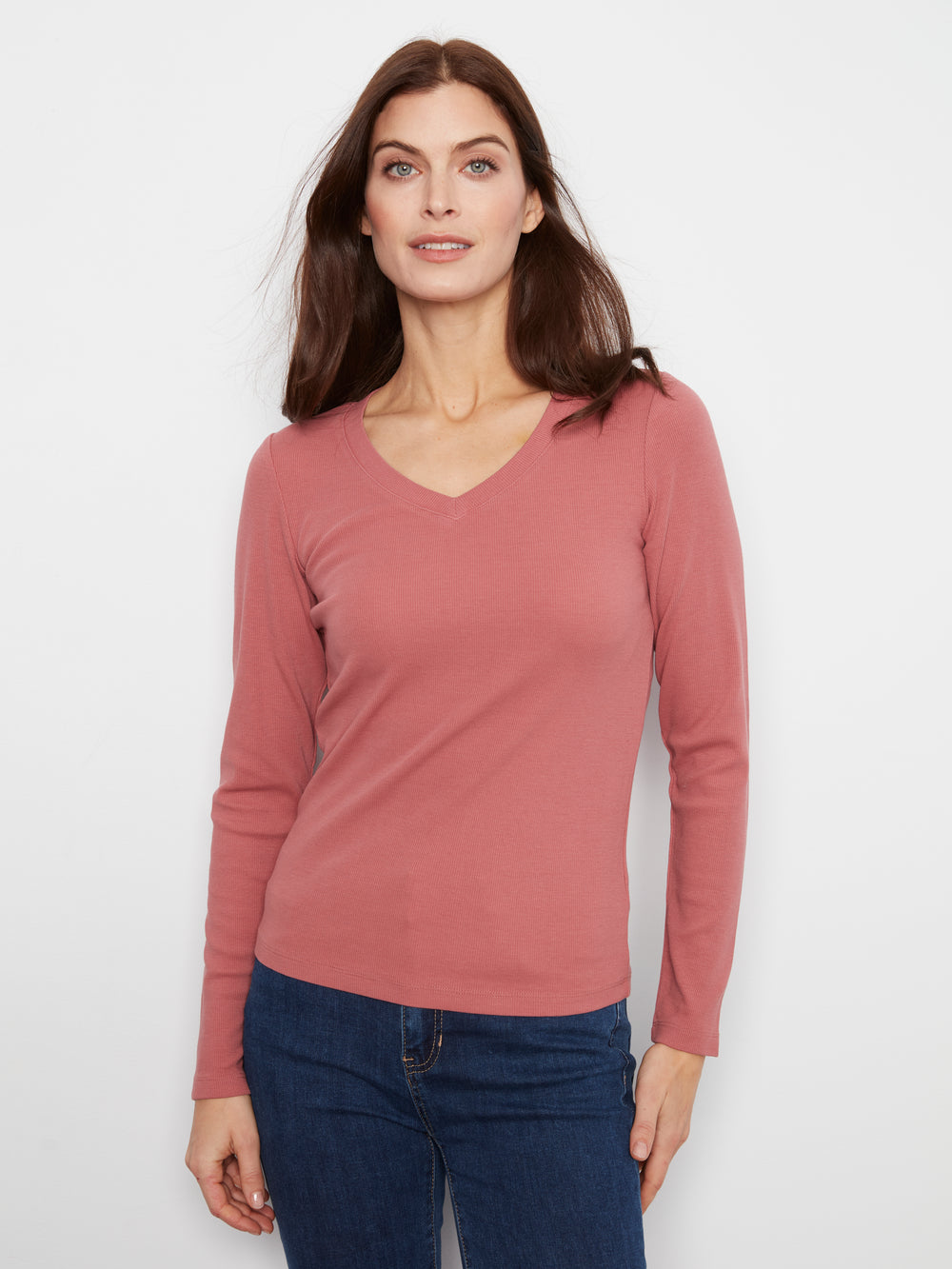 Woman wearing a pink long-sleeve top and blue jeans on a white background