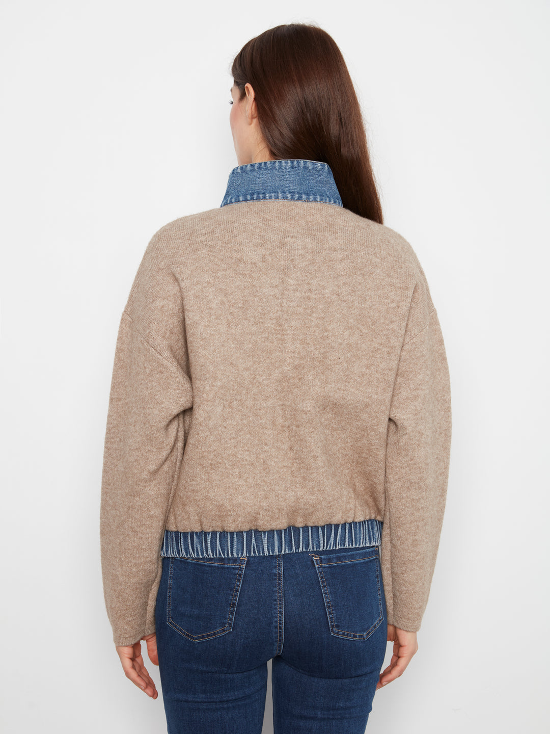 Woman wearing a beige sweater with denim trim on a white background