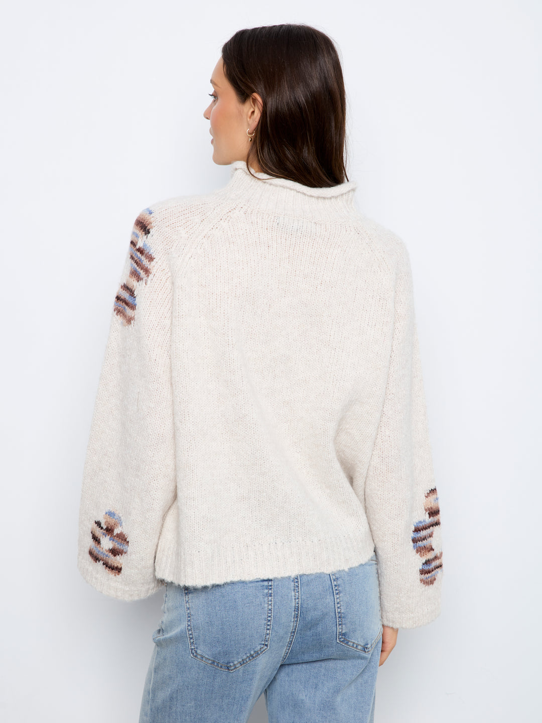 A woman shown from the back wearing a cream-colored, fuzzy knit sweater with distressed details on the sleeves, paired with light blue jeans, against a plain white background.