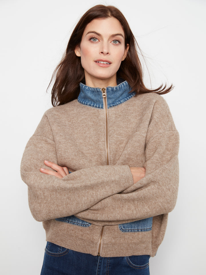 A woman wearing a beige knit zip-up sweater with a blue denim mock neck collar, denim patch pockets, and a matching blue denim hem, paired with blue jeans against a plain white background.
