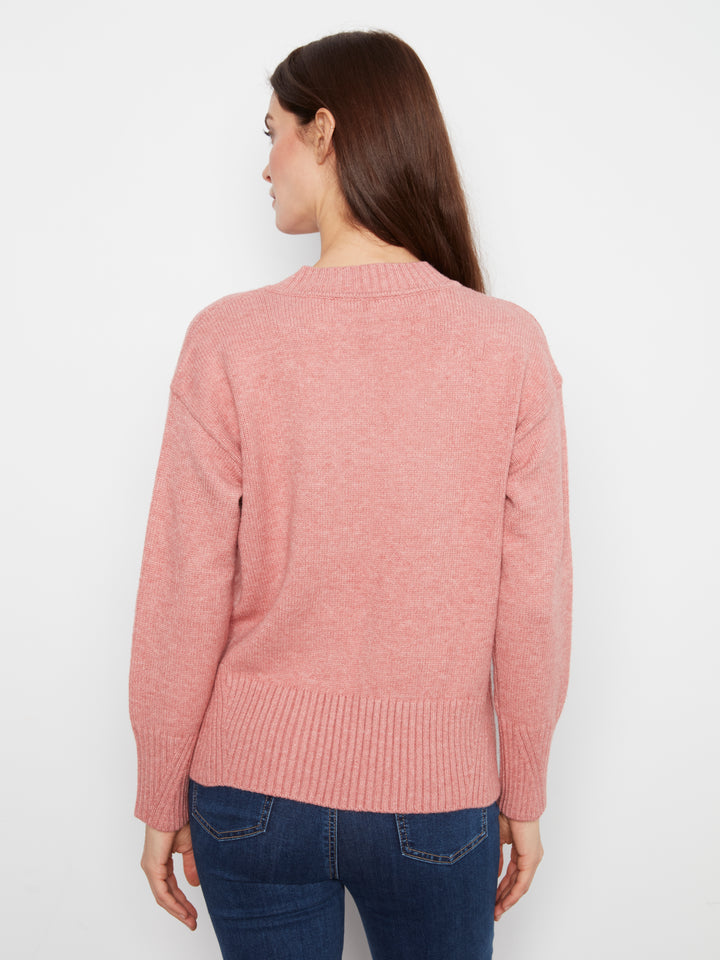 Woman wearing a pink sweater and blue jeans against a white background