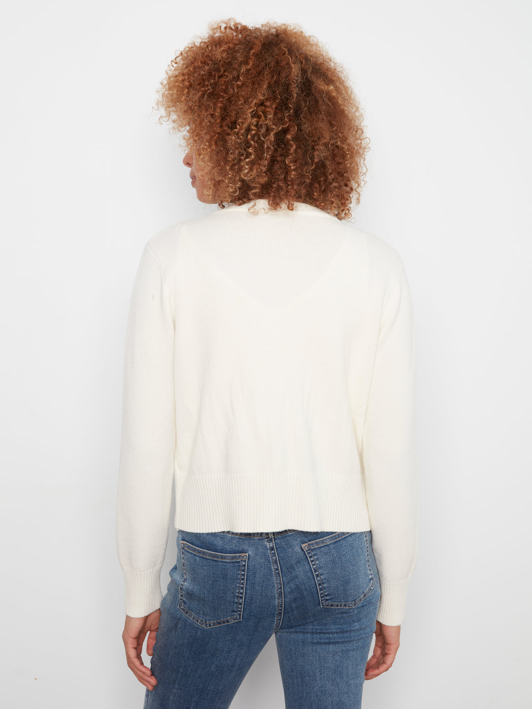 A person shown from the back wearing a cream-colored long-sleeve knit top and blue jeans against a plain white background.