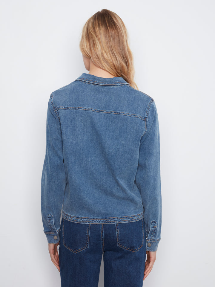 A woman viewed from the back wearing a medium-wash blue denim jacket and dark blue jeans against a plain white studio background.