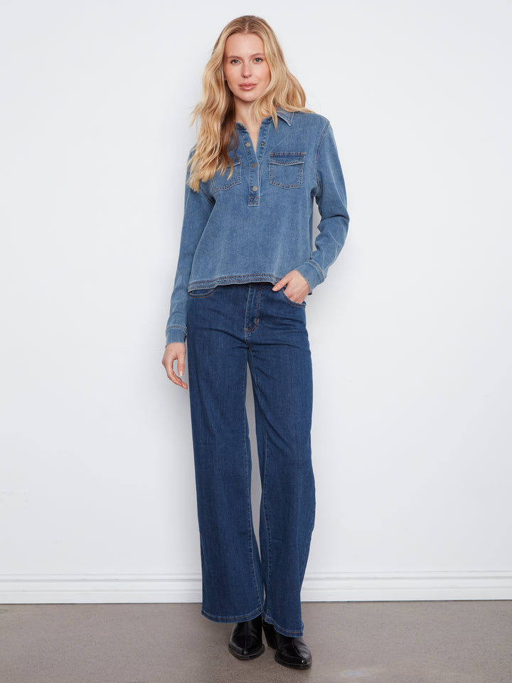 A woman modeling a blue denim long-sleeve button-up shirt and matching dark blue wide-leg jeans against a plain white wall.