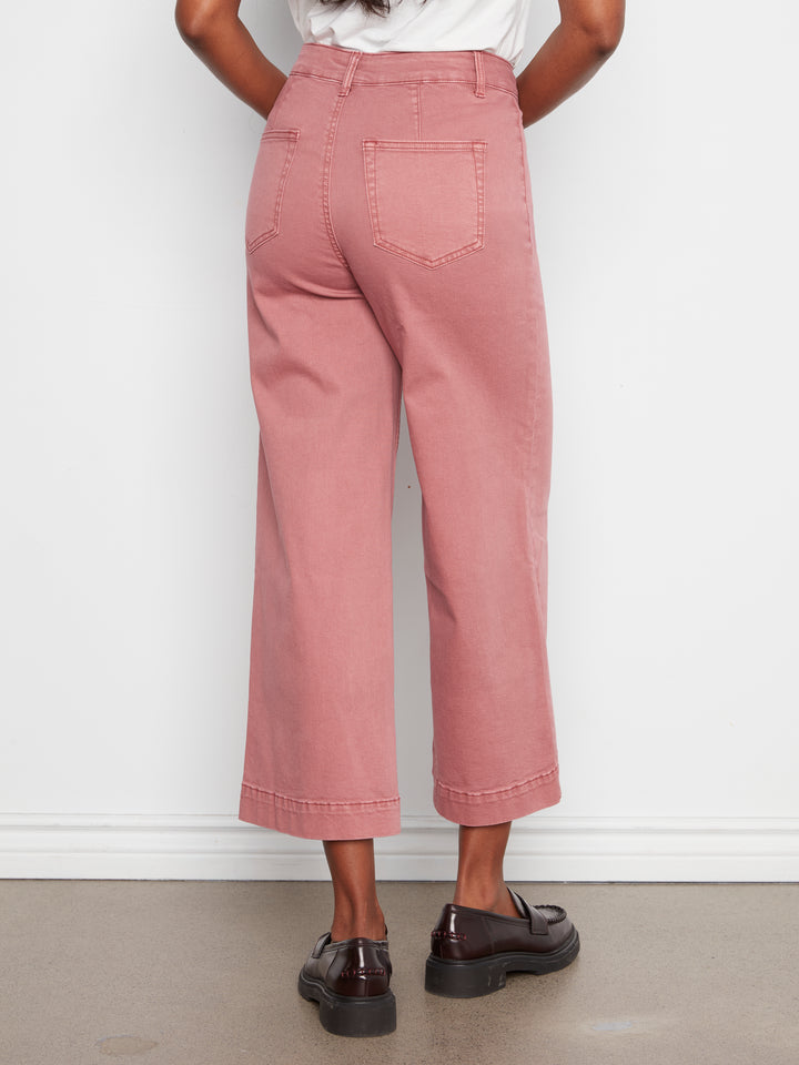 A person shown from the back wearing dusty rose cropped wide-leg jeans with rolled hems, paired with a white top and dark brown leather loafers, standing against a white wall.