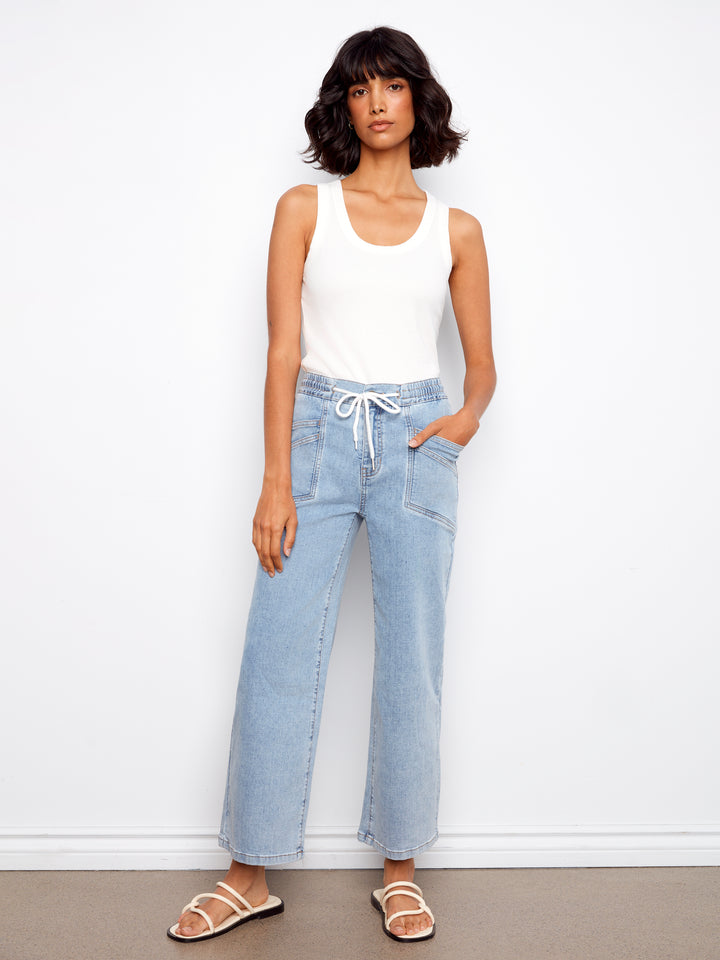 Woman wearing a white tank top and light blue jeans against a white background