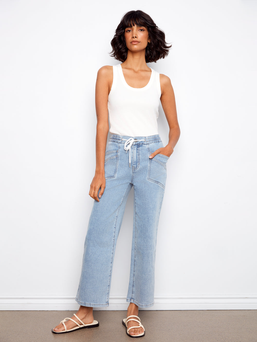 Woman wearing light blue jeans and a white tank top against a white background