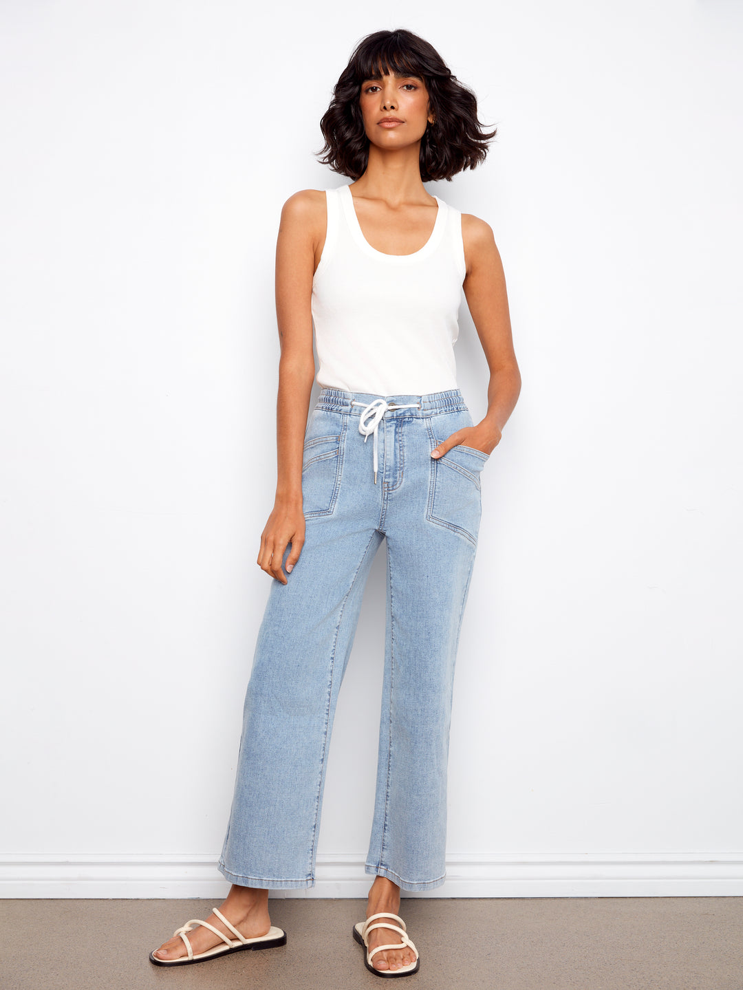 Woman wearing light blue jeans and a white tank top against a white background