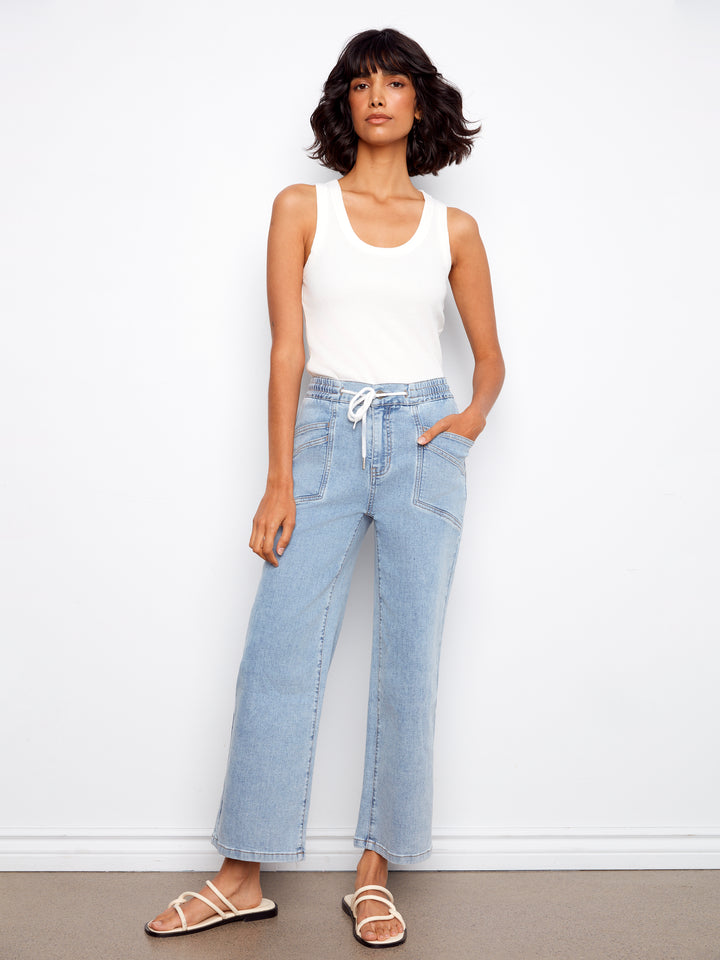 Woman wearing light blue jeans and a white tank top against a white background