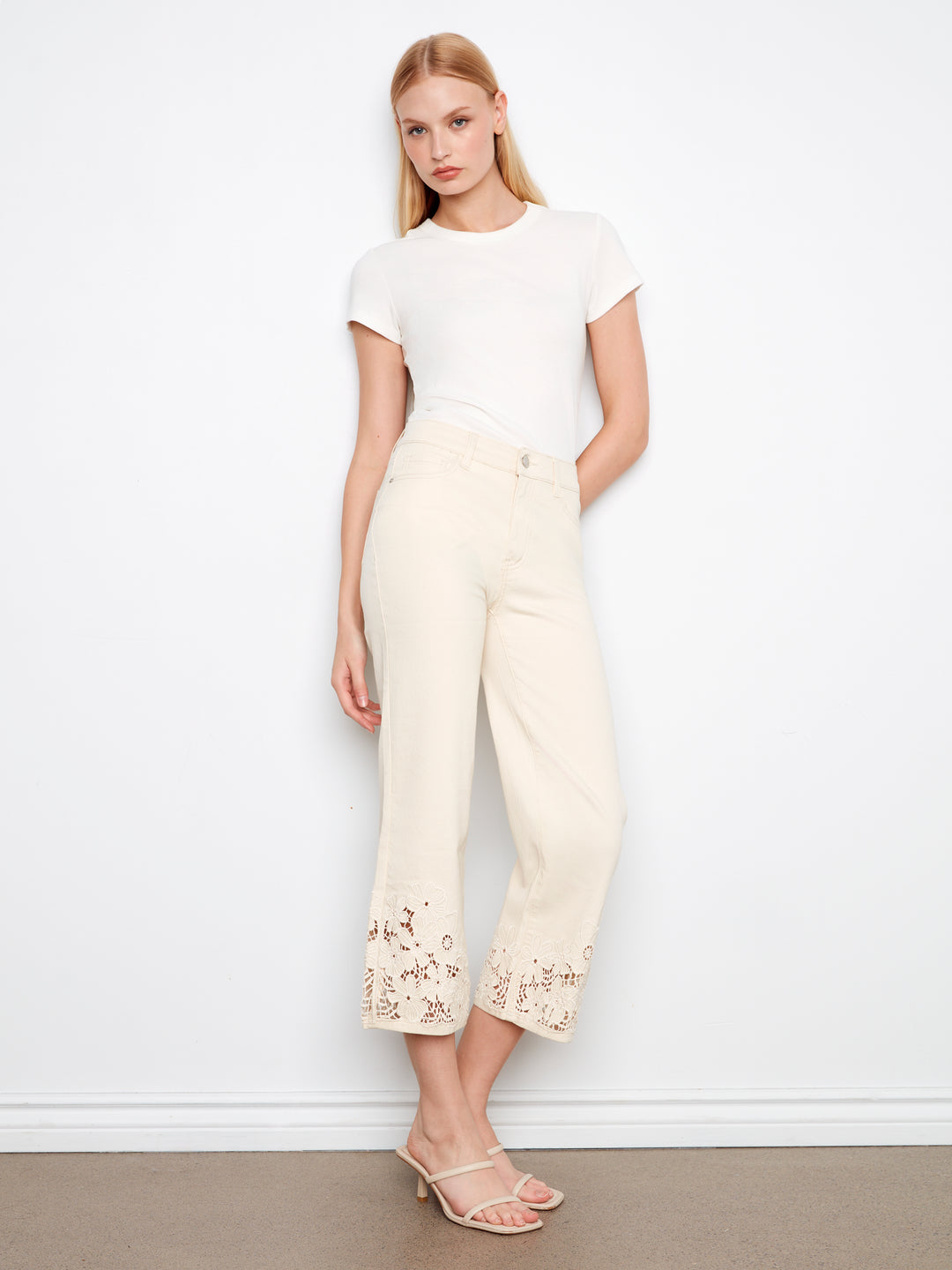 Woman wearing a white top and cream pants with floral embroidery against a white background