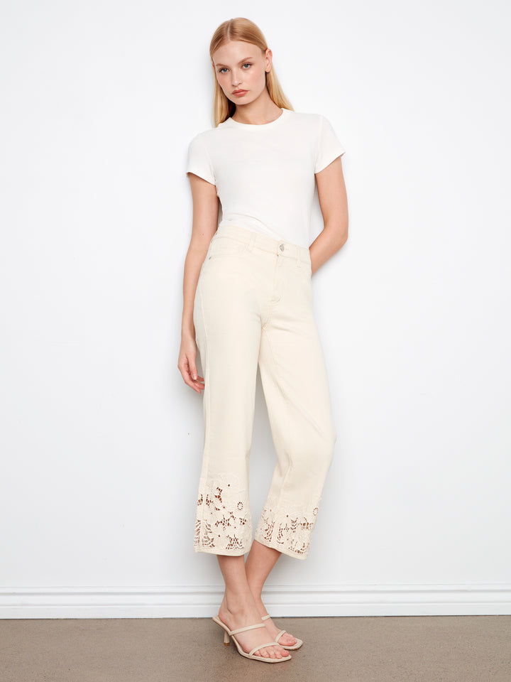 Woman wearing a white top and cream pants with floral embroidery against a white background