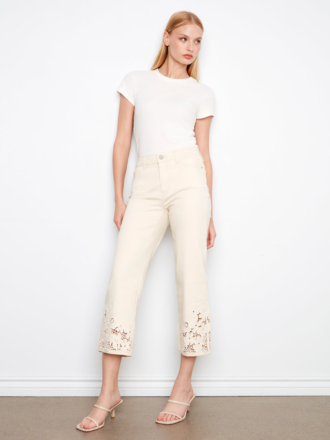 Woman wearing a white t-shirt and cream-colored pants against a plain background