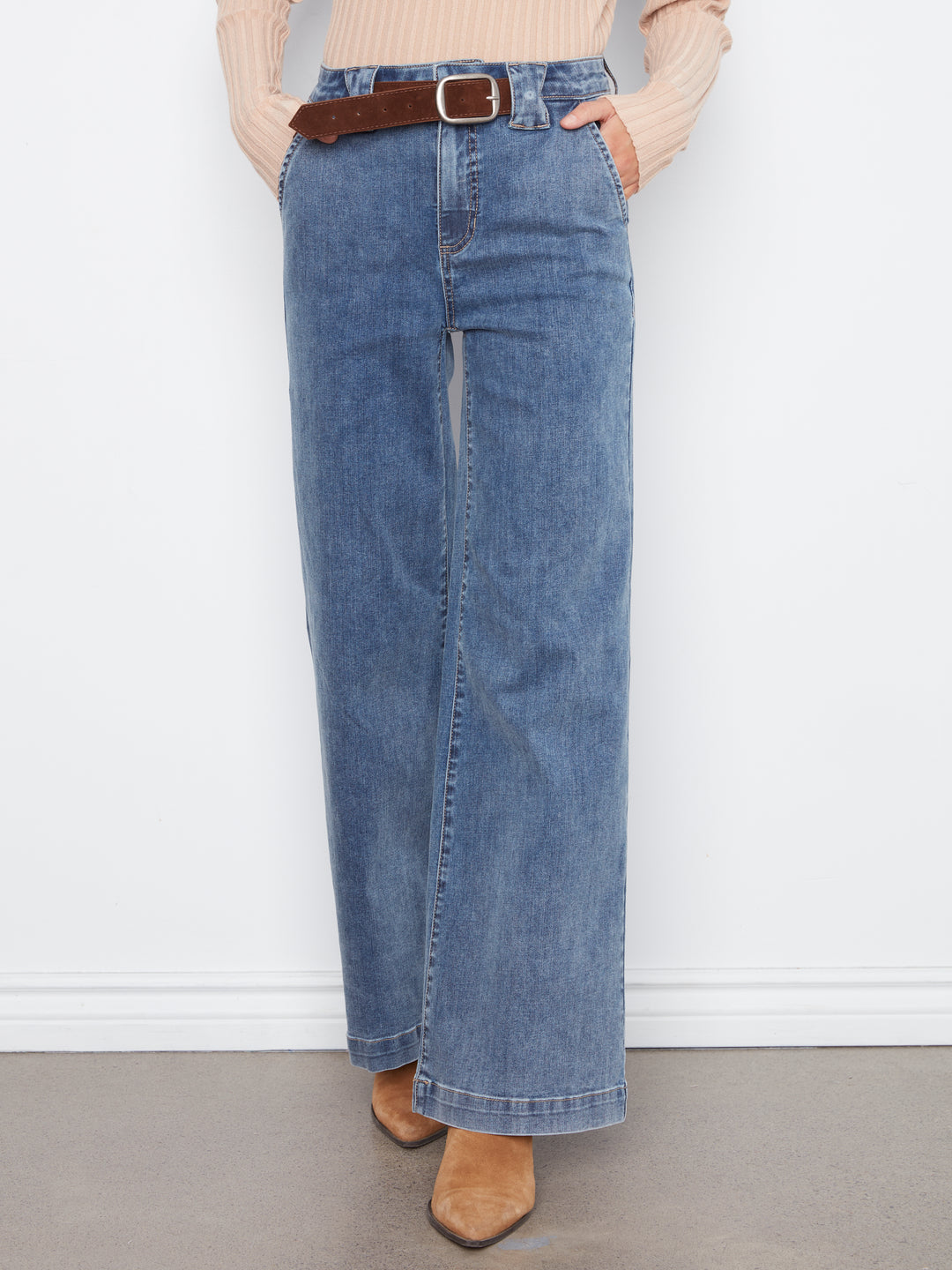 Person wearing blue jeans with a belt on a plain background