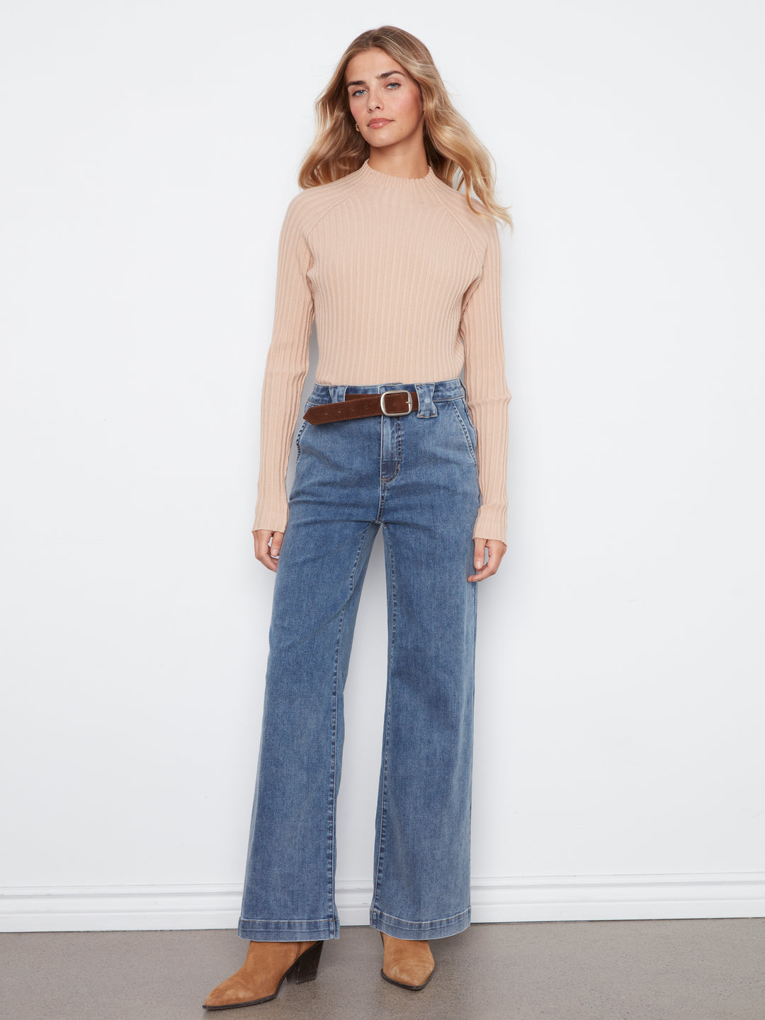 Woman wearing a beige sweater and blue jeans against a white background