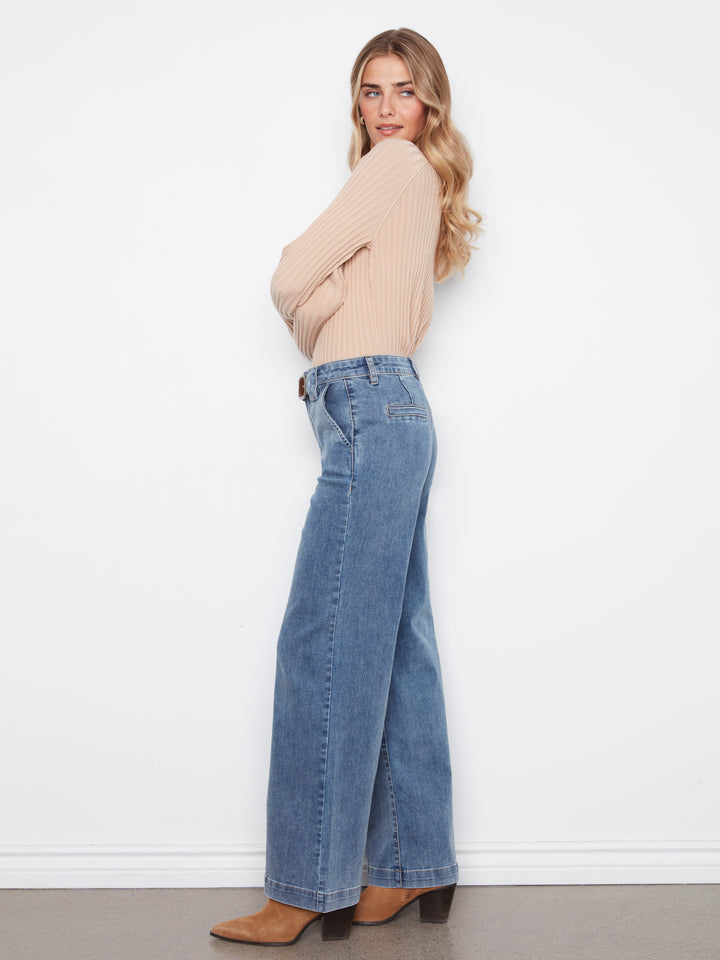 Woman wearing a beige sweater and blue jeans against a white background