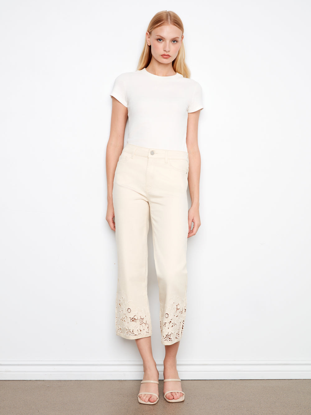 Woman wearing a white top and cream pants with floral embroidery against a white background