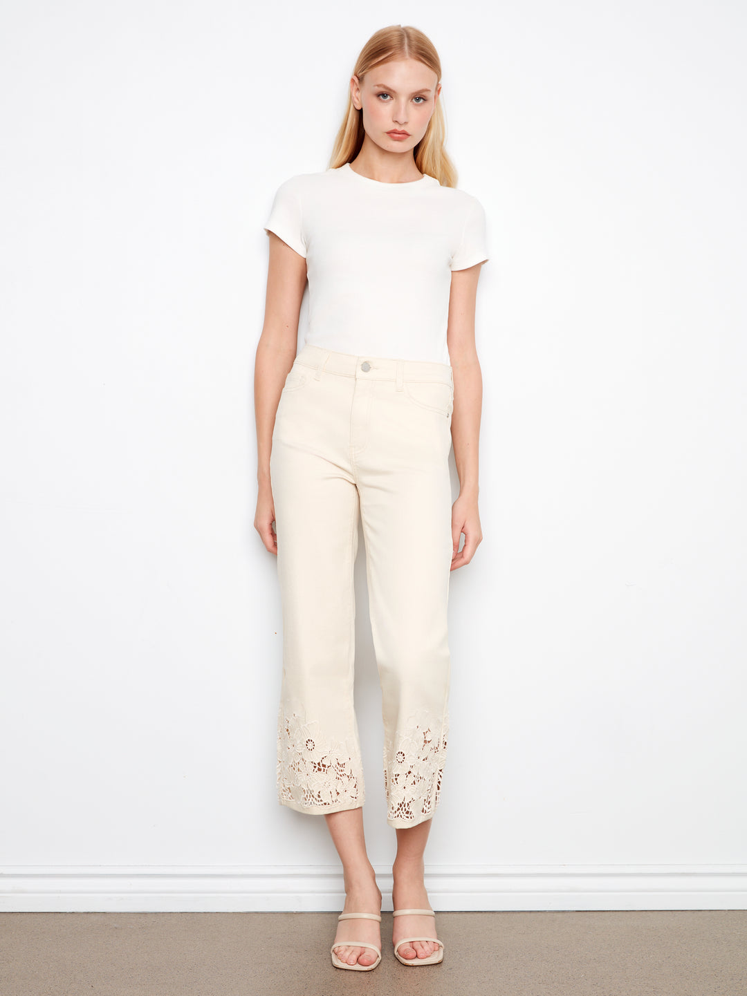 Woman wearing a white top and cream pants with floral embroidery against a white background